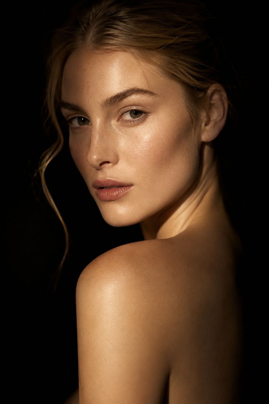 Editorial beauty portrait, fair skin, lit in warm gold against black